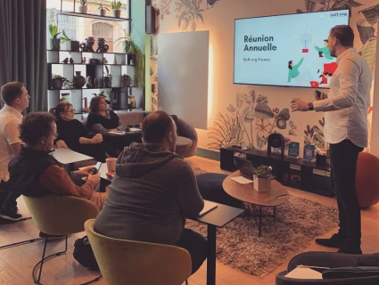 Réunion annuelle d’équipe animée par un intervenant devant un écran de présentation dans un espace de travail chaleureux