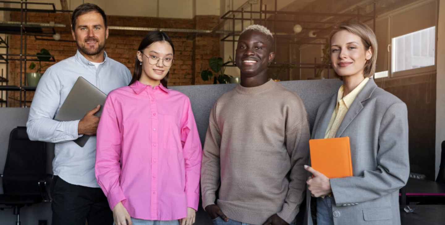 Groupe diversifié de quatre collègues souriants, debout ensemble dans un bureau moderne, illustrant la collaboration en entreprise et la diversité au travail.
