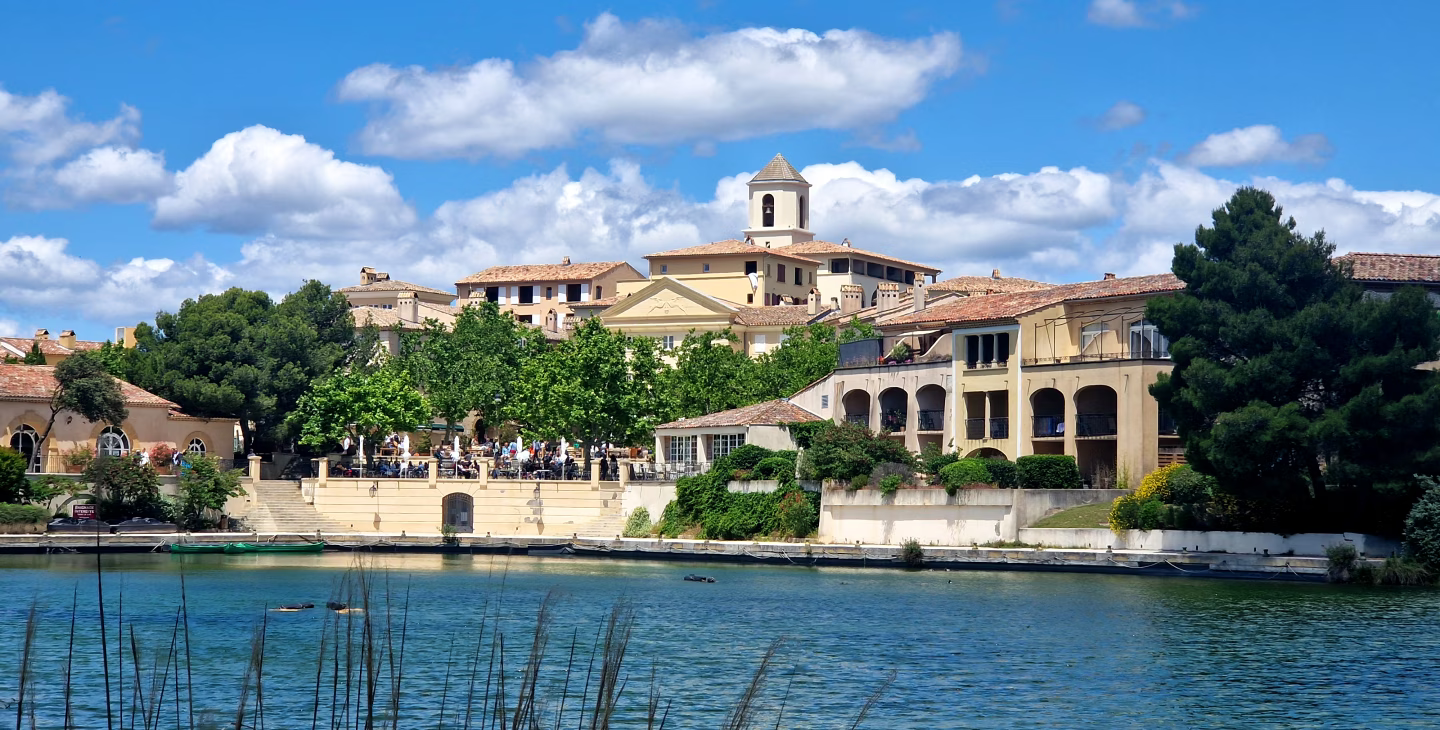 Village provençal typique avec maisons en pierre et tuiles rouges au bord d’un lac sous un ciel bleu ensoleillé