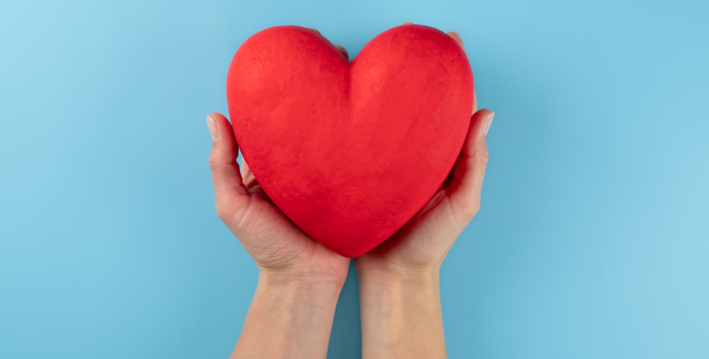 Deux mains tenant un cœur rouge en symbole de don, de générosité ou de bienveillance sur fond bleu clair