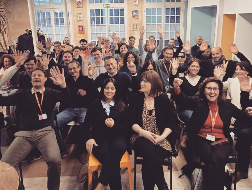 Photo de groupe d’une équipe ERT Intégration enthousiaste, bras levés, lors d’un événement interne