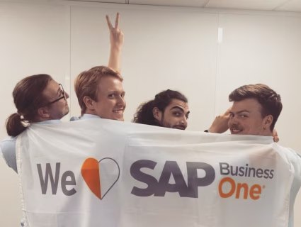 Quatre collaborateurs souriants tenant une bannière “We love SAP Business One” dans un bureau