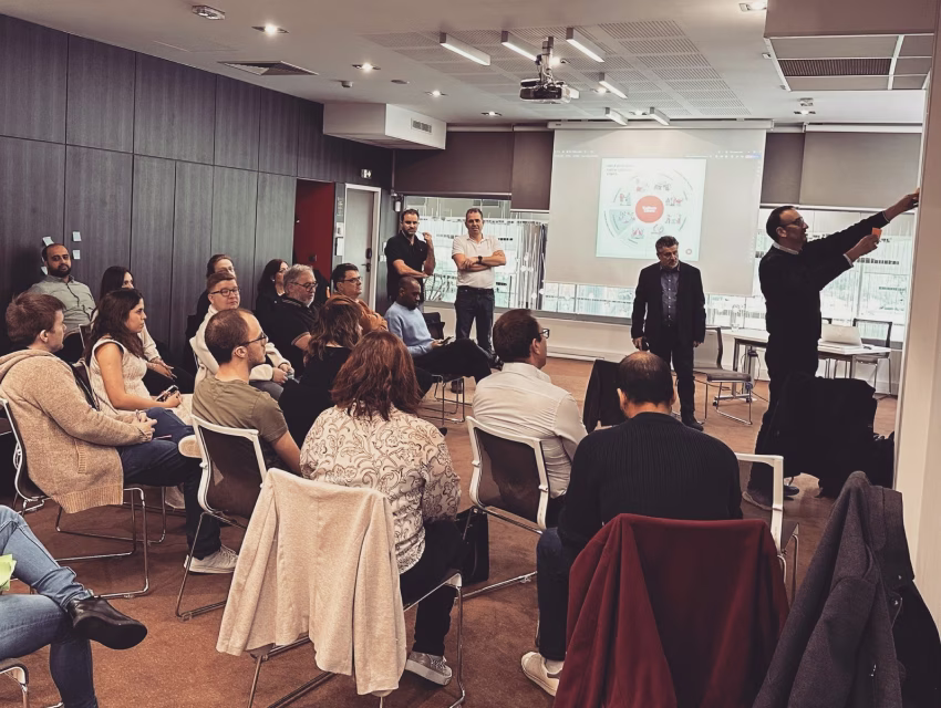 Groupe de collaborateurs en atelier participatif dans une salle de séminaire avec intervenants et supports projetés